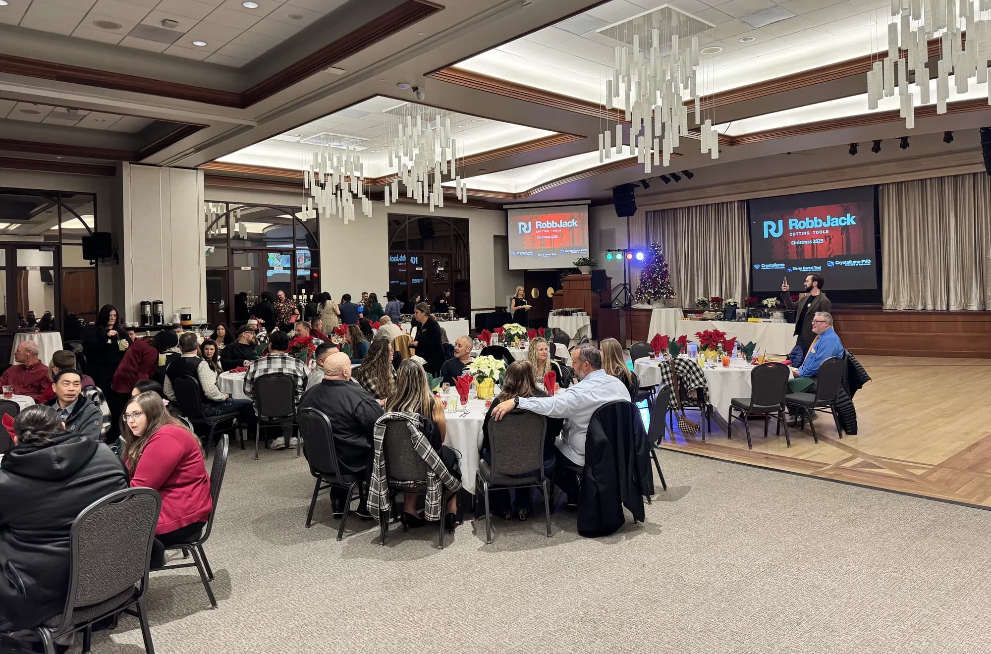 The RobbJack team and their families gathered at round tables at the company Christmas party, with the RobbJack logo on the screens.